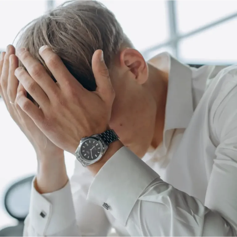 PCA NWA mental health services - A man in a white shirt sits with his head in his hands, appearing stressed or frustrated, possibly contemplating EMDR Therapy for relief.