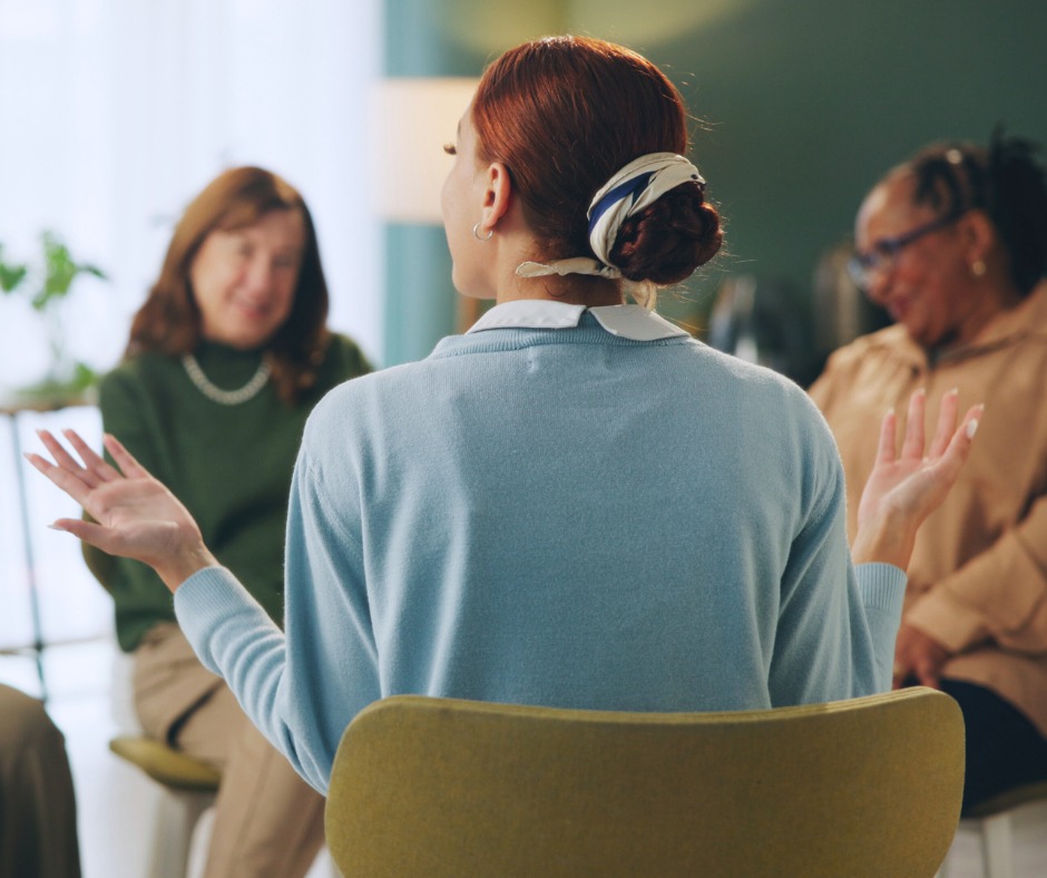 PCA NWA mental health services - A woman with a scarf in her hair discusses EMDR Therapy with two women while seated in a group, indoors.