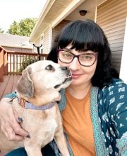 PCA NWA mental health services - A woman with dark hair and glasses sits on a wooden deck, holding a small tan dog that looks up at her.