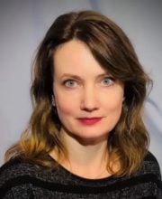 PCA NWA mental health services - A woman with shoulder-length brown hair and blue eyes, wearing a black striped top, poses against a plain light background.