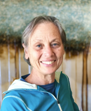 PCA NWA mental health services - A middle-aged person with short gray hair and a teal jacket is smiling in front of an abstract, nature-themed background.