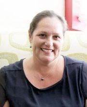PCA NWA mental health services - A woman with tied-back hair and a dark top sits on a patterned couch, smiling at the camera.